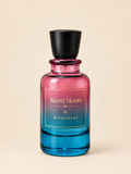 A glass perfume bottle with a black cap, featuring a pink-to-blue gradient body and a gold label that reads 'Secret bloom By Binyousaf', set against a solid beige background.